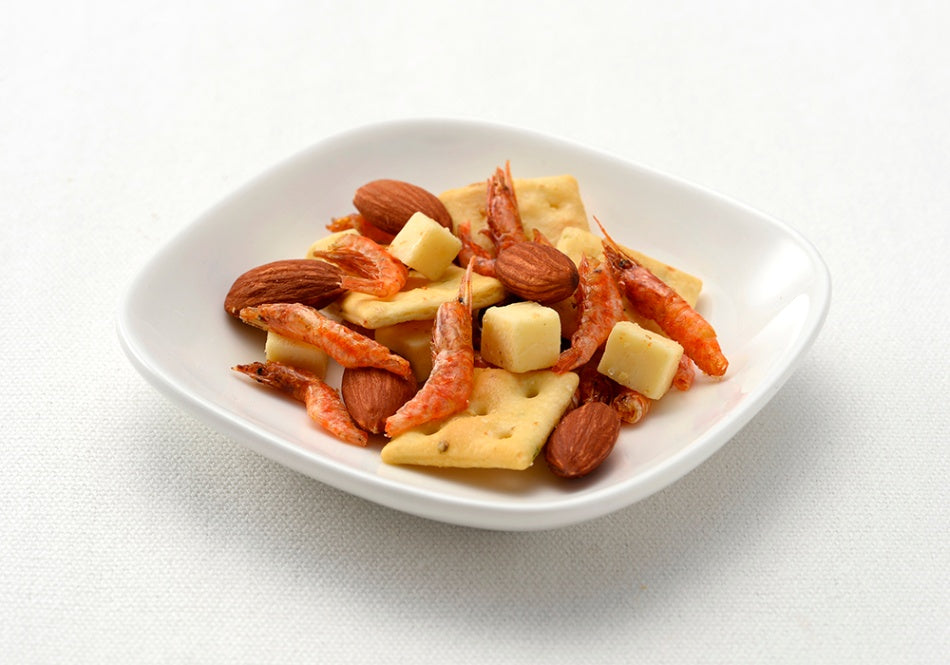 Snack mix with shrimp, cheese cubes, vegetable crackers, and almonds on a white plate.