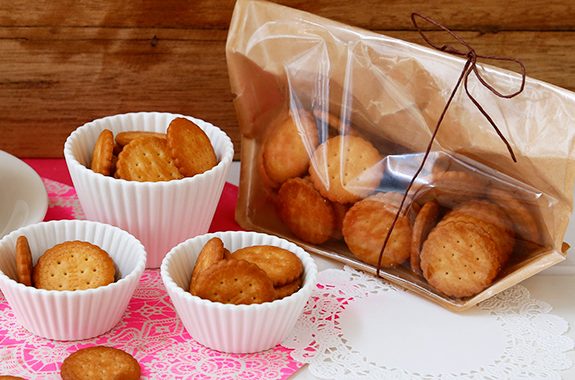 Oyatsu Millet Biscuits in ceramic cups and a decorative package on a pink doily, showcasing their crunchy texture and savory flavor.