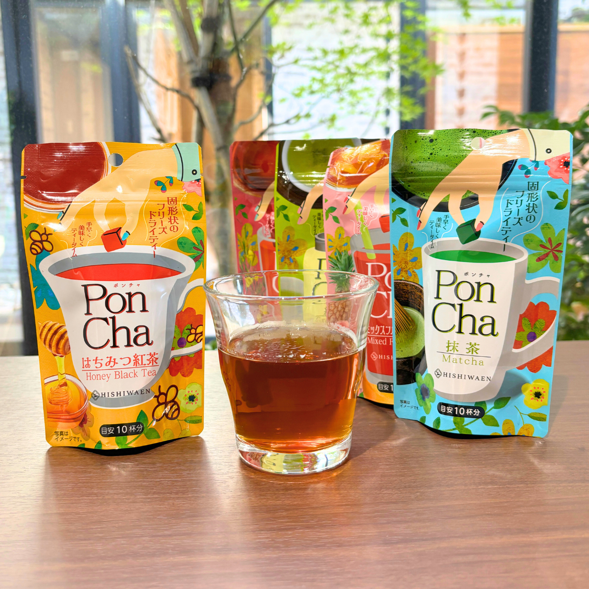 PonCha Honey Black Tea, Matcha, and more flavors freeze-dried tea, with a glass of brewed tea on a wooden table.
