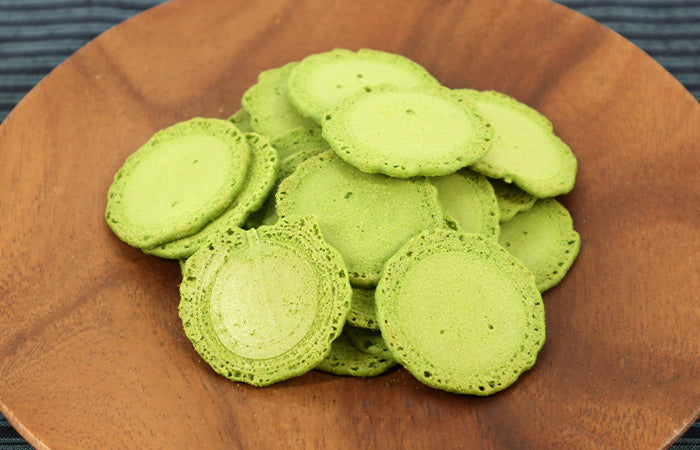 Bite-size matcha rice crackers on a wooden plate, showcasing their bright green color and preserving the fragrance of matcha green tea.