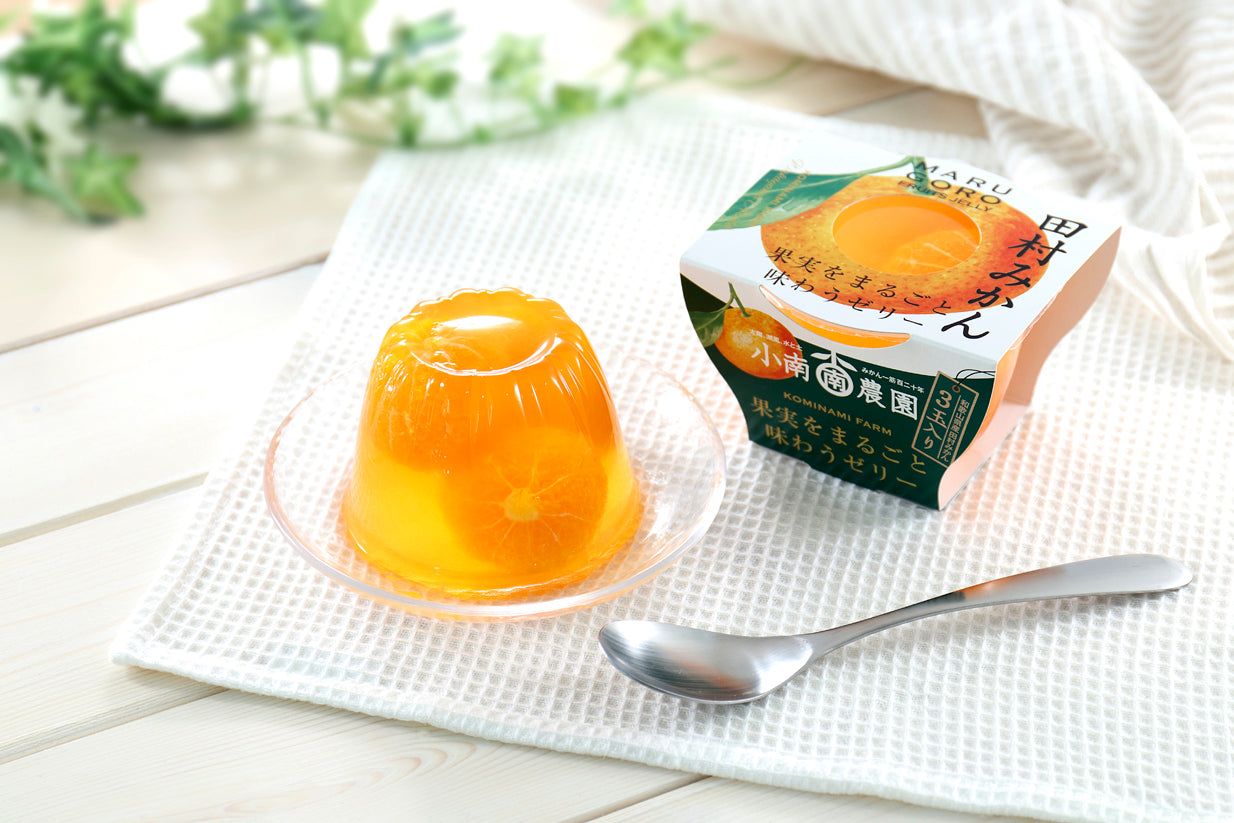 Marugoto Jelly Fruit with whole mandarin orange displayed on a plate, next to product packaging, set on a white background with spoon.