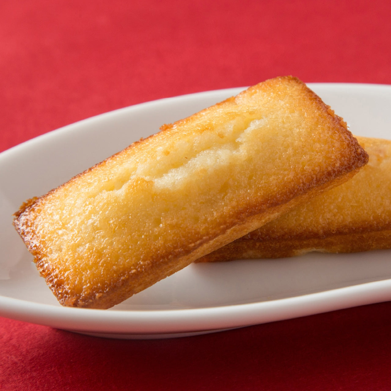 Nanae Apple Financier on a white plate, made with Hokkaido apples, showcasing a golden-brown finish. Includes allergens: dairy, egg, wheat, apple, almond.