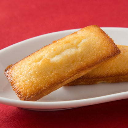 Nanae Apple Financier on a white plate, made with Hokkaido apples, showcasing a golden-brown finish. Includes allergens: dairy, egg, wheat, apple, almond.