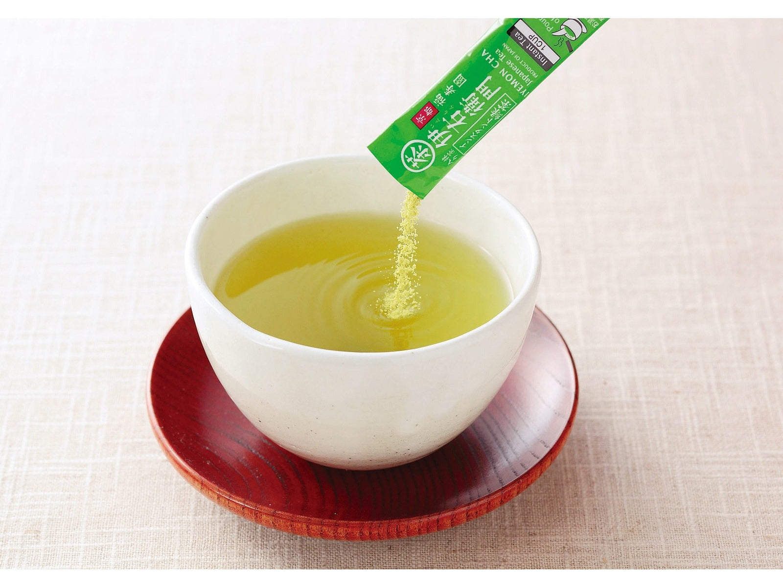 IYEMON Instant Green Tea being poured from stick into a white cup on a red saucer, capturing the essence of Japanese teapot brewed tea.