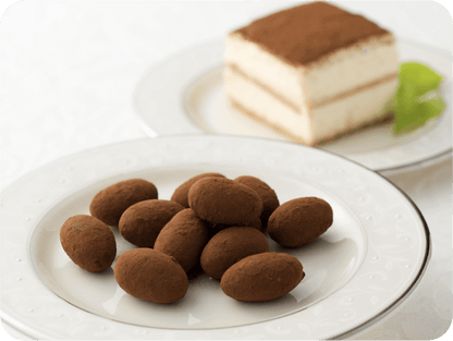 Plate of tiramisu chocolates with almonds and mascarpone, dusted with cocoa, next to a slice of tiramisu cake.