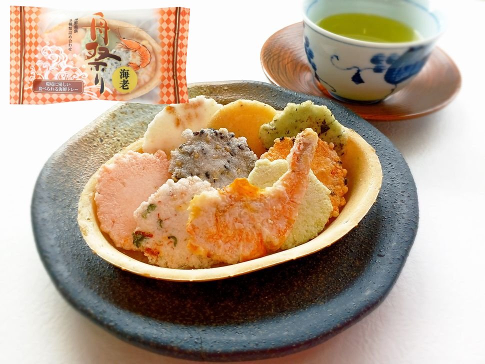 Assorted SUGI Funamatsuri shrimp and octopus rice crackers in an edible tray beside a cup of green tea.