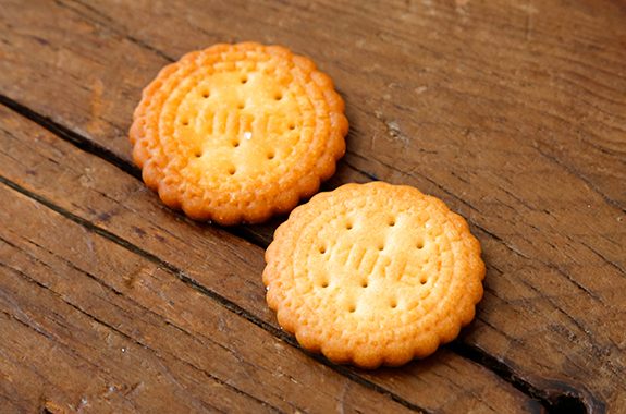 Two savory millet biscuits on a wooden surface, showcasing their crunchy texture and golden-brown color.